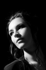 The girl in the fashion style with professional make-up looks to the side on a close-up on a black background in a low key