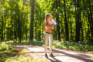 Fitness beautiful woman drinking water and sweating after exercising on summer hot day in park. Female athlete after work out.