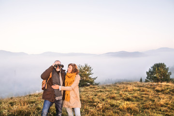 Obraz premium Senior couple with binoculars on a walk in an autumn nature.