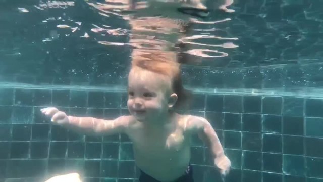 Happy smiling toddler is jumping and diving under the water in the swimming pool. An underwater shot.