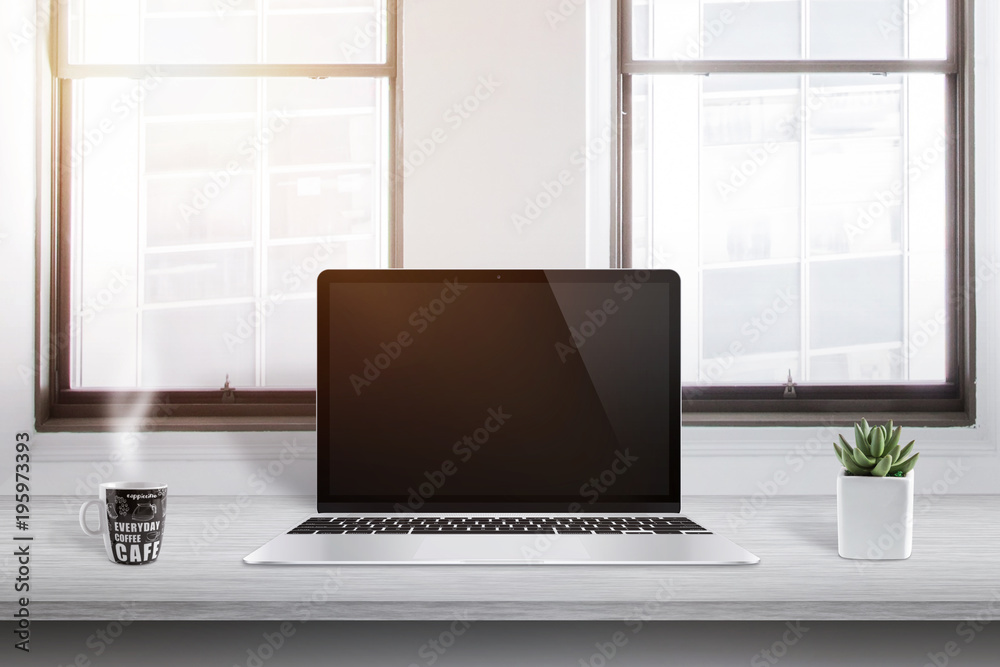 Poster laptop computer on office desk with cup of coffee and plant beside. sun enters through the window in
