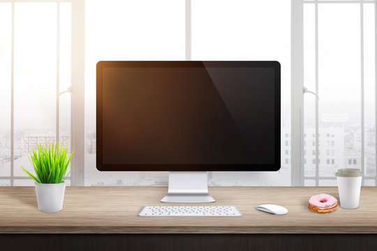 Blank computer display in office or workplace. Plant, coffee and donut beside. Morning sun light in background.