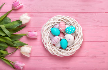 Easter eggs in a wicker basket and bouquet tulips on wooden background.Easter holiday concept.