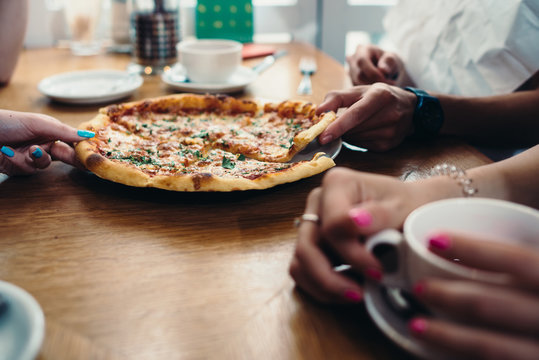 Close-up image of delicious pizza and hands taking slices in Italian restaurant