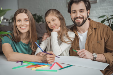Obraz premium smiling parents and daughter drawing with felt-tip pens and looking at camera