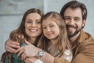 portrait of smiling parents and daughter hugging and looking at camera