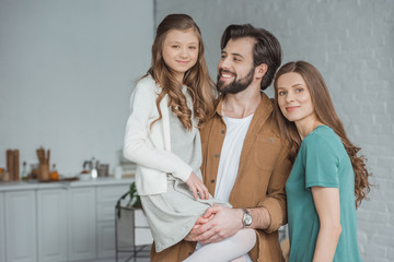 Fototapeta premium smiling parents and daughter standing together in kitchen