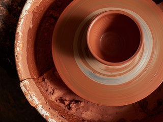 production process of pottery. mug of red clay on a potter's wheel.