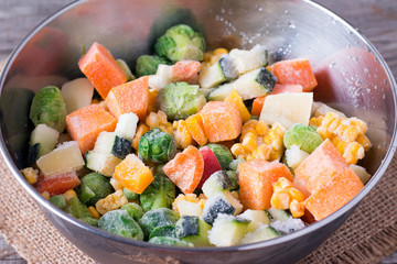 Frozen vegetables in bowl on wooden table background.