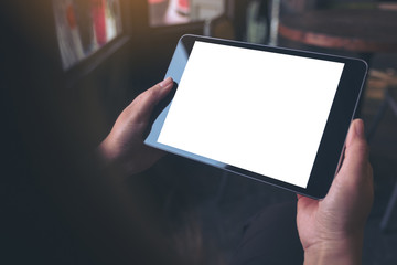 Mockup image of hands holding black tablet pc with blank white desktop screen in vintage wooden cafe