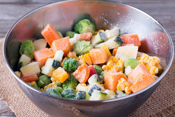 Frozen vegetables in bowl on wooden table background.