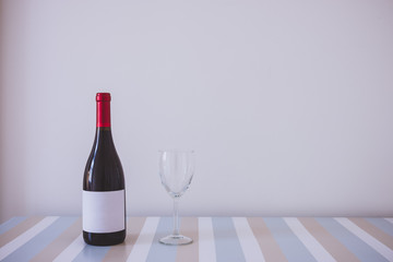 Wine bottle with wine glass on a table over white wall