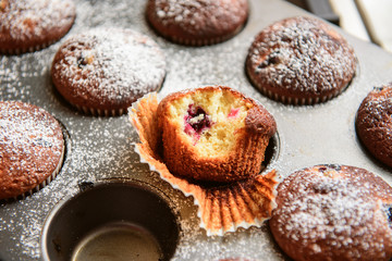 homemade muffins with forest berries one of which is bitten on a baking sheet in the oven