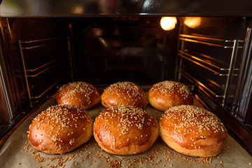homemade burger rolls sprinkled with sesame seeds are baked in the oven