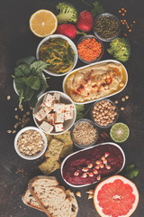 Vegan food background. Vegetarian snacks: hummus, beetroot hummus, green peas dip, vegetables, cereals, tofu. Top view, dark background, copy space.