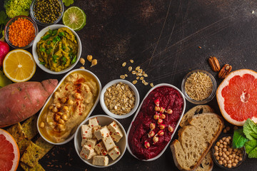 Vegan food background. Vegetarian snacks: hummus, beetroot hummus, green peas dip, vegetables, cereals, tofu. Top view, dark background, copy space.