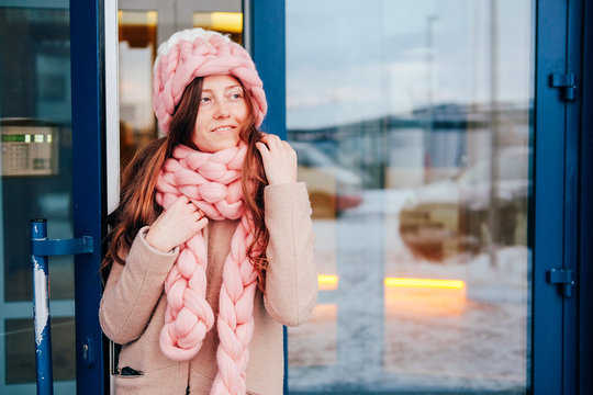Cute young woman in knitted hat and scarf leaving the building