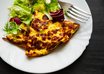 omelet with fresh mixed salad leaves in a plate on dark wooden background