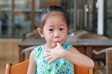 Adorable little asian girl sucking thumb at restaurant.