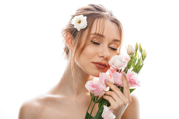 Obraz na płótnie Canvas Sensual young woman 20s with tied auburn hair holding and smelling beautiful eustoma flowers, isolated over white background