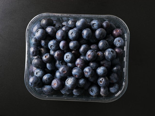 Plastic box with fresh blueberries on dark background.