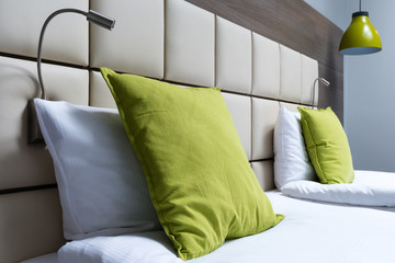 Green pillow, reading lamps and leather bed headboard in modern bedroom