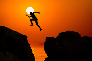 Man jumping over precipice between two rocky mountains at sunrise. Freedom, risk, challenge, success.
