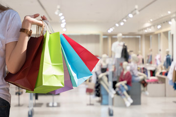 Attraction woman hand holding shopping bags in one hand with blur cloth shop background - Shopping Concept