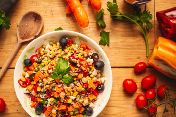A view of a spelled dish on wooden background with some ingredients around: carrots, peppers,...