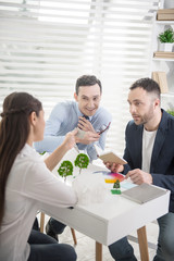 Pleasant talk. Attractive joyful young dark-haired man smiling and discussing a project with his colleagues while sitting at the table