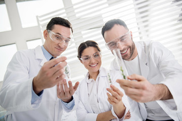 Inspiration. Content professional experienced scientists smiling and wearing uniforms and holding test tubes