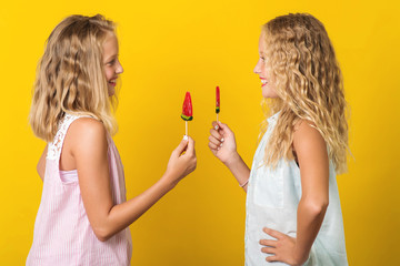 Two handsome young girls or sisters posing with lollipop on yellow background.