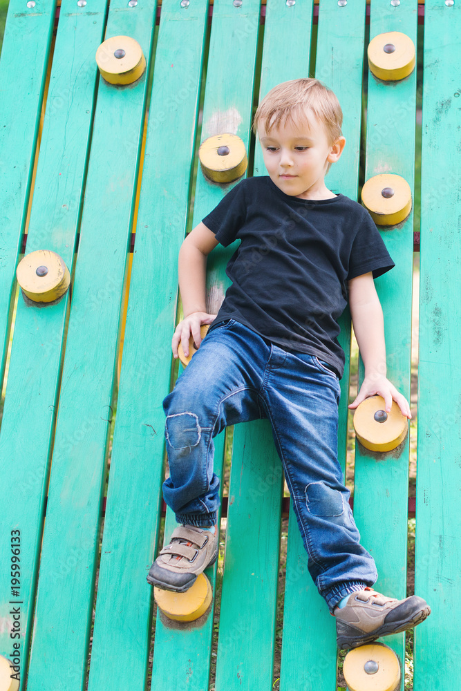 Wall mural cute little boy having fun and climbing on outdoor playground.