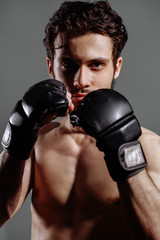 closeup shot of young naked boxer wearing protecting gloves. throwing puches in a boxing ring. grey background © alfa27