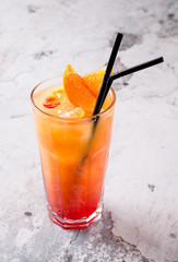 Delicious cocktail with orange juice and Red Tequila Sunrise, ice cubes in a glass on gray background restaurant. Exotic red summer drink. Bar alcohol menu, enjoy. Homemade lemonade