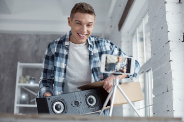 Fototapeta premium Wonderful sound. Handsome content professional well-built blogger holding loudspeakers and smiling while making a video