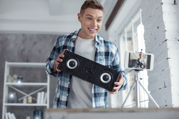 Modern loudspeakers. Good-looking alert professional well-built blogger holding loudspeakers and smiling while making a video