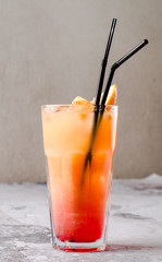 Delicious cocktail with orange juice and Red Tequila Sunrise, ice cubes in a glass on gray background restaurant. Exotic red summer drink. Bar alcohol menu, enjoy. Homemade lemonade