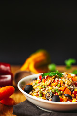 A view of a spelled dish on wooden background with some ingredients around: carrots, peppers, tomatos, parsley and oil