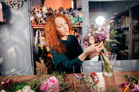 image of young Caucasian hardworking flower asistant concentrating on her work, holding a bounch of natural flowers at store