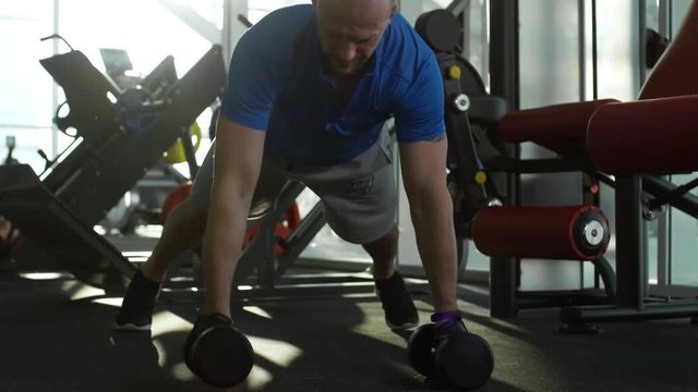 Front view of mature man performing plank row with dumbbells at the gym