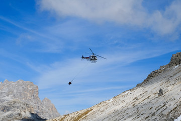 Fototapeta na wymiar Hubschrauber transportiert in den Bergen eine Betonwanne zu einer schwer zugänglichen Baustelle