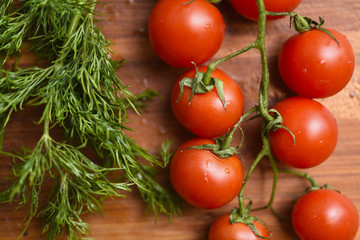 Cherry tomatos and heap of dill on wooden surface