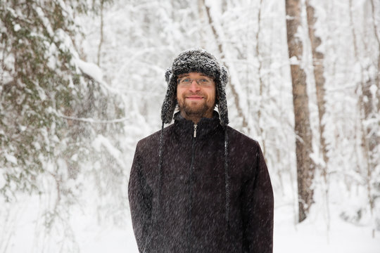 Man in fur winter hat with ear flaps smiling portrait. Extreme in the forest
