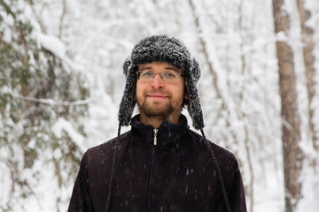 Man in fur winter hat with ear flaps smiling portrait. Extreme in the forest
