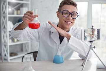 Delighted. Good-looking alert fair-haired teenager wearing a uniform and glasses and holding test tubes while doing an experiment