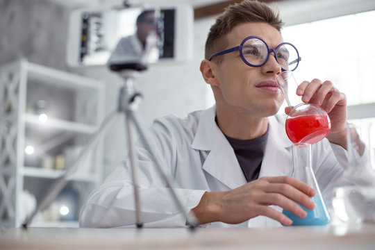 Strange smell. Nice serious fair-haired teenager wearing a uniform and glasses and holding test tubes while doing an experiment