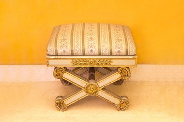 Classic retro foot stool with striped upholstery near the yellow wall