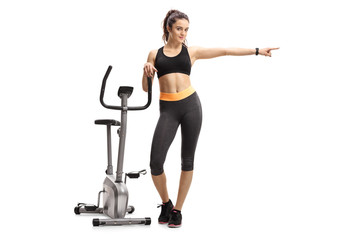 Obraz premium Fitness woman leaning on an exercise bike and pointing