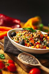 A view of a spelled dish on wooden background with some ingredients around: carrots, peppers, tomatos, parsley and oil